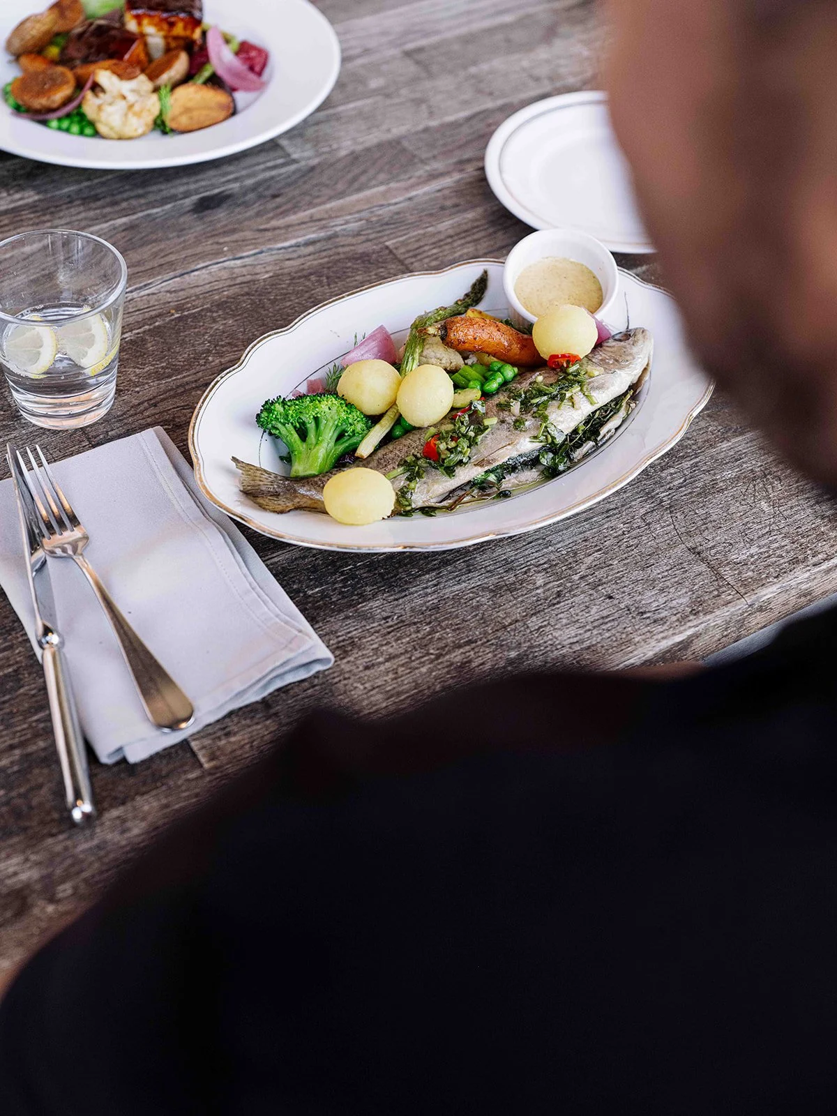 Poisson farci avec des légumes, pommes de terre, brocoli, asperges, et accompagnement de sauce dans un plat oval traditionnel posé sur une table en bois
