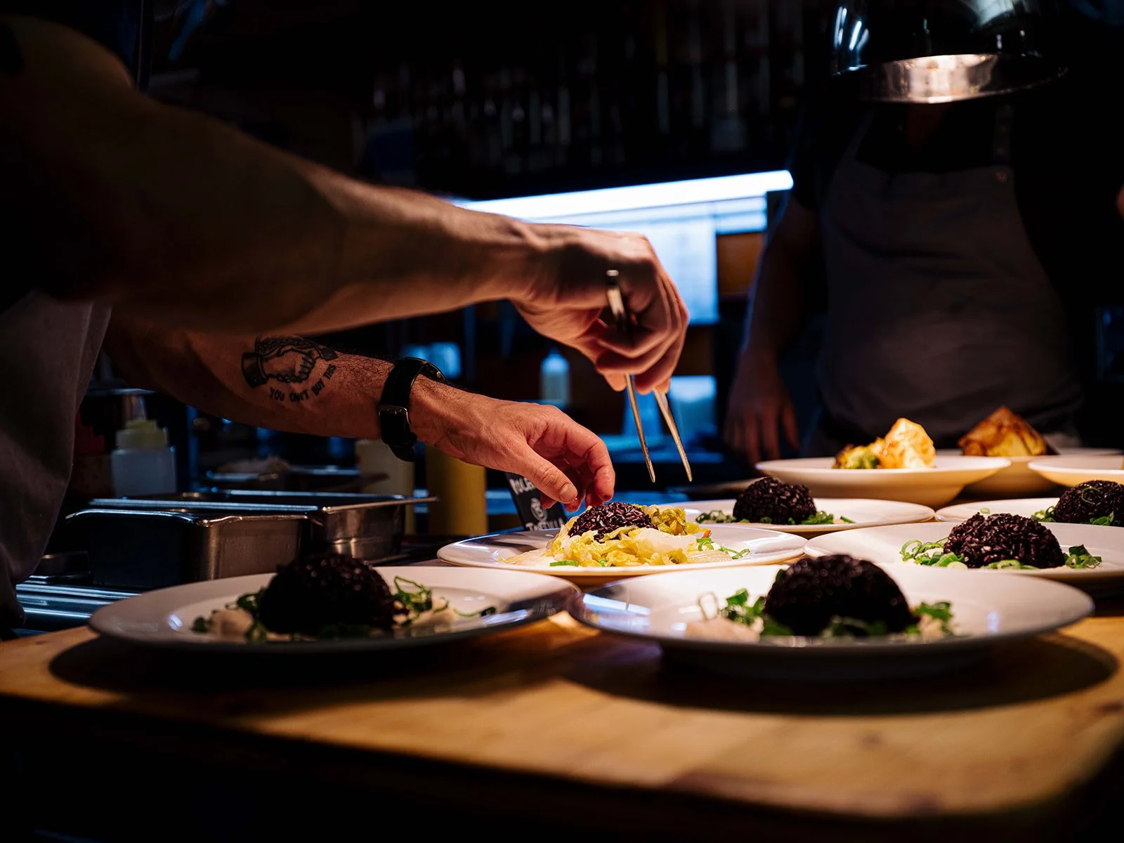 Cuisinier décorant une assiette avec des ingrédients noirs, jaunes et verts dans une cuisine professionnelle