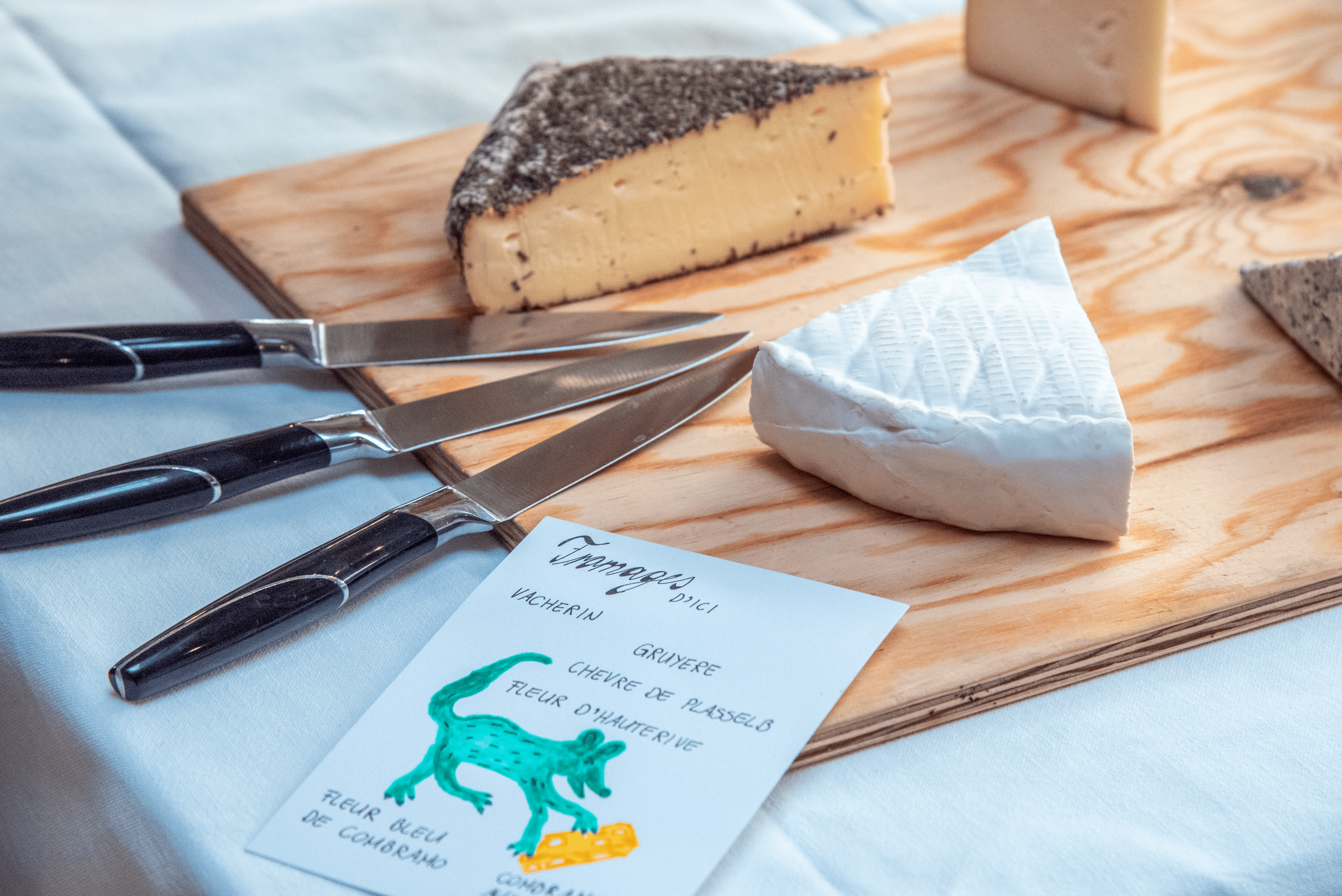 Plateau en bois avec différents types de fromages, un couteau, une fourchette et un sirop ou une confiture. Aucun contexte supplémentaire visible.