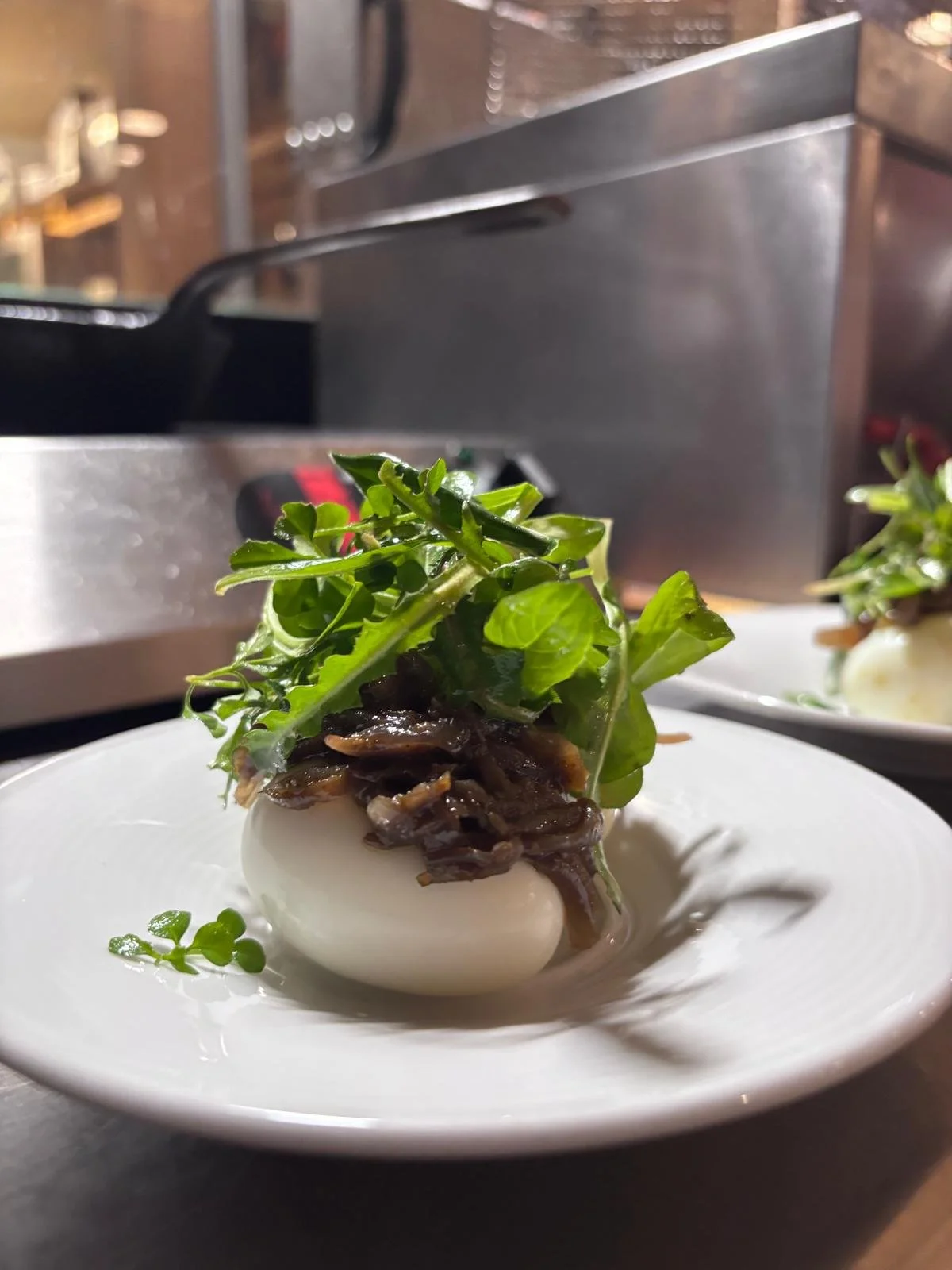 Œuf mollet garni de salade verte, oignons caramélisés et microgreens, présenté sur une assiette blanche.