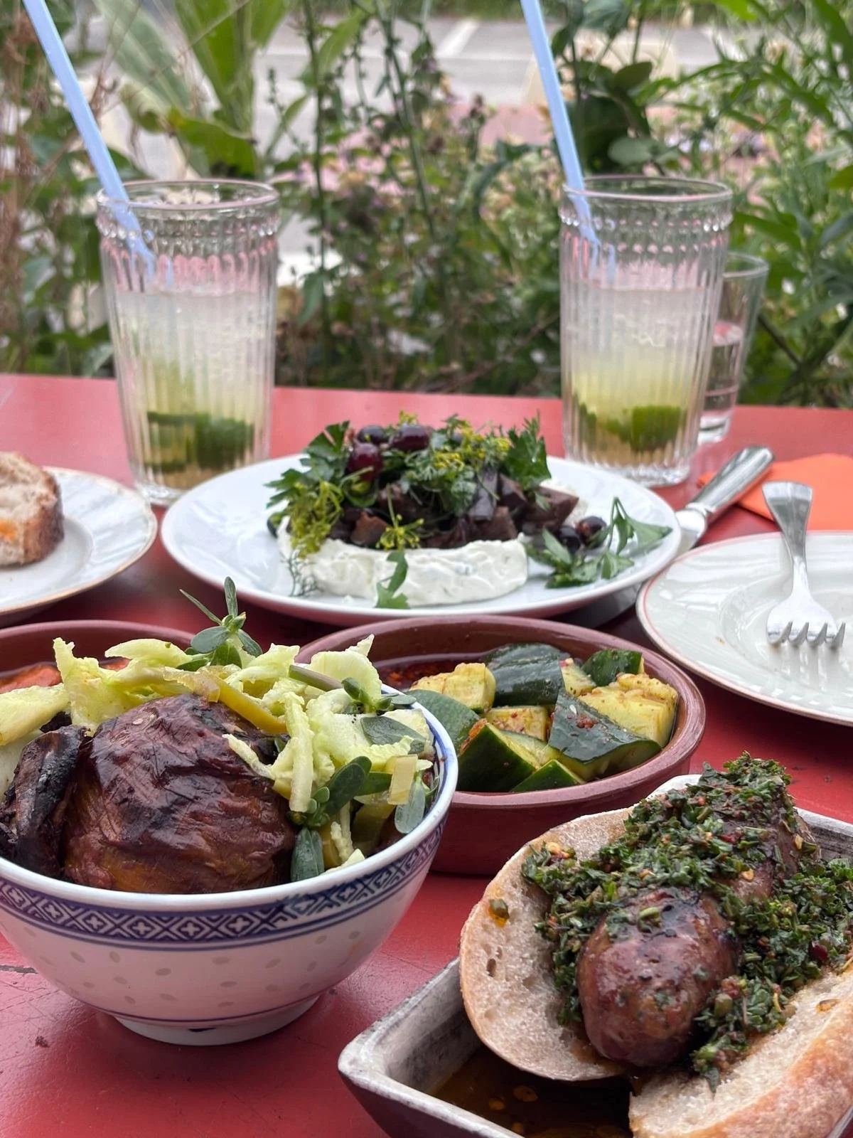 Repas méditerranéen avec salades, légumes et boissons rafraîchissantes sur une table en extérieur.