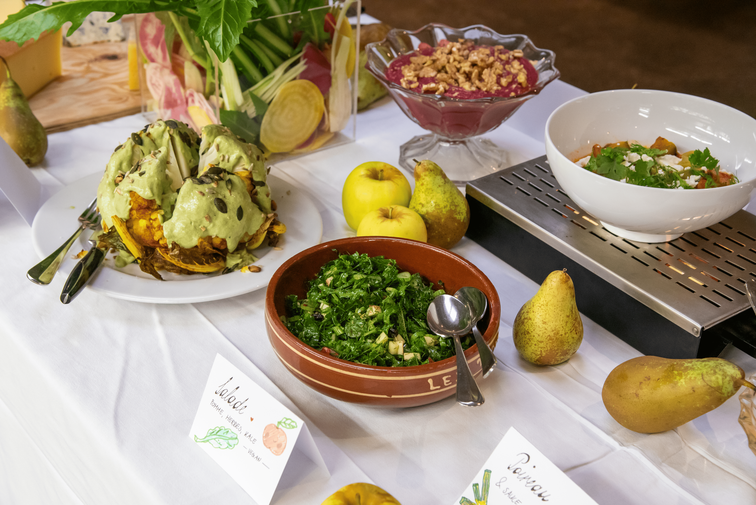 Présentation de plats végétariens et fruits sur une table, avec des salades, des pommes, des poires et des desserts.