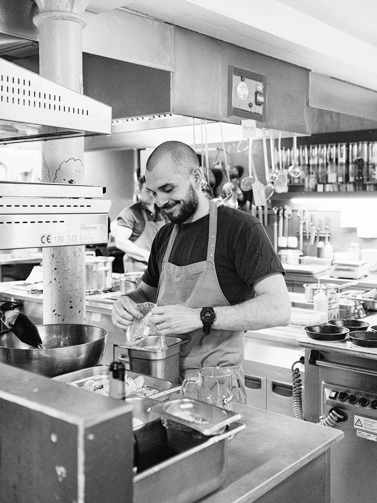 Un homme souriant prépare de la nourriture dans une cuisine de restaurant ou de grande cuisine.