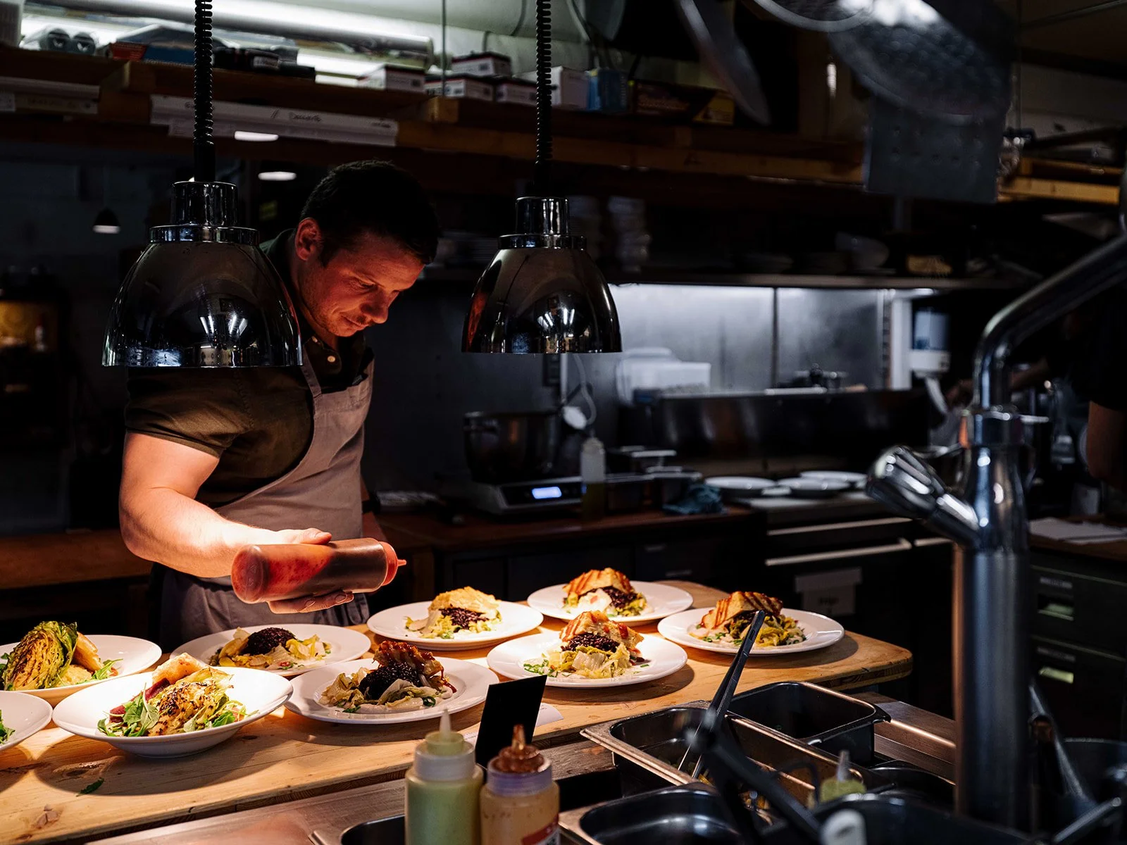 Un chef en cuisine, en train de préparer des plats dans une cuisine professionnelle, avec plusieurs assiettes de nourriture sur le plan de travail.