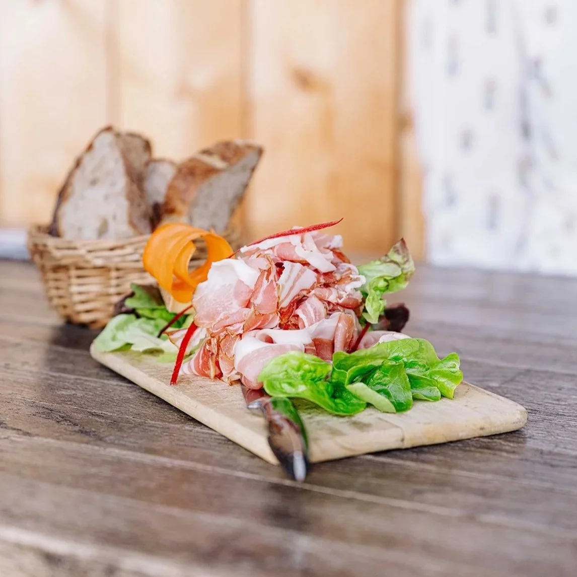 Assiette de viande crue et de salade avec du pain en arrière-plan.