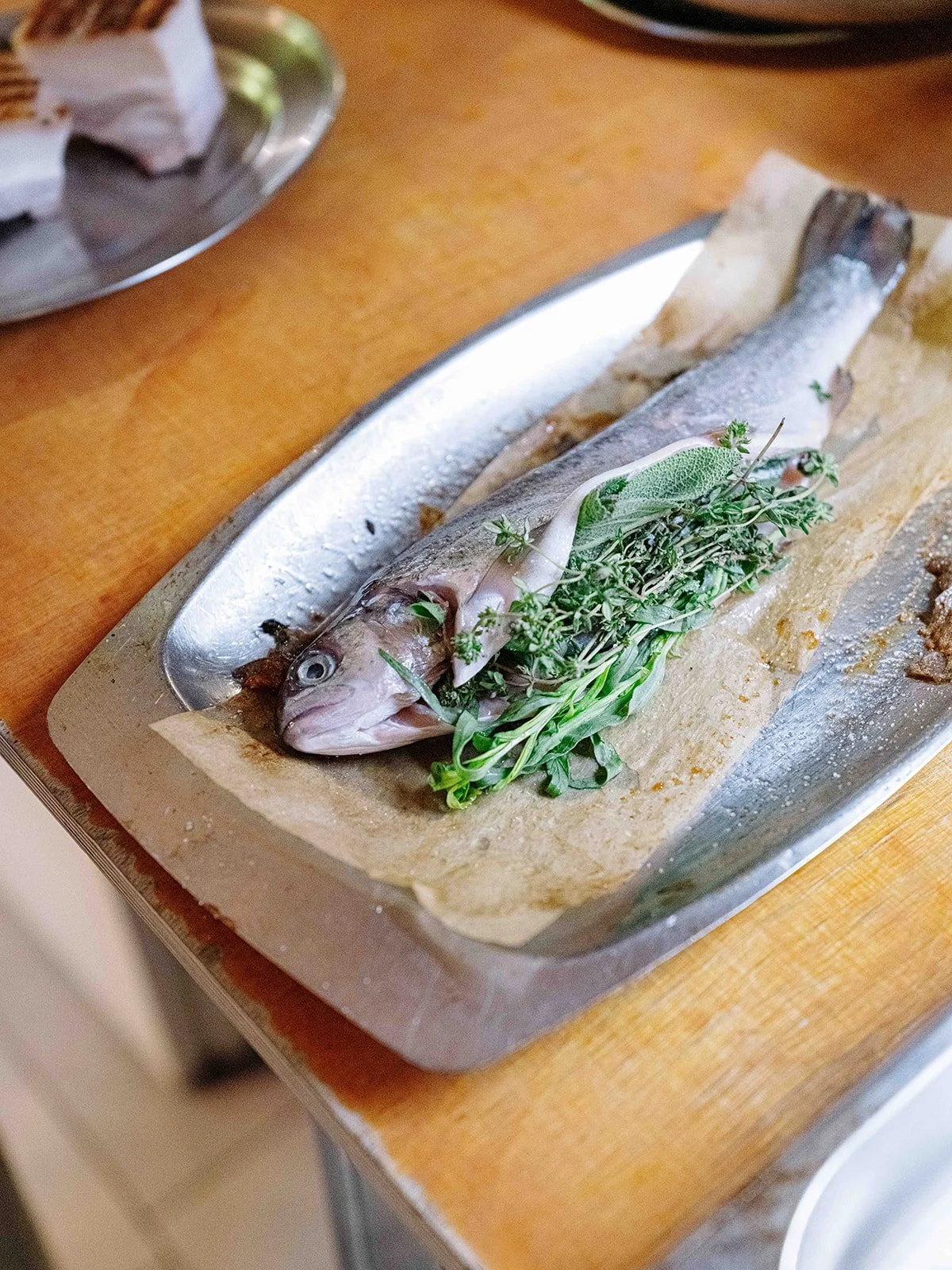 Poisson entier sur une plaque de cuisson, garni de fines herbes comme du thym, du romarin, et une feuille de sauge, prêt à être cuit.