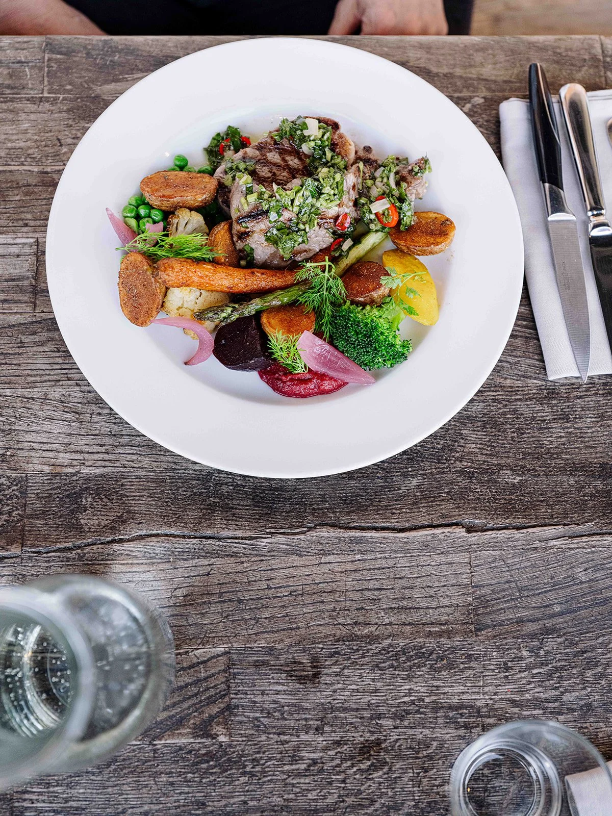 Assiette de nourriture avec viande et légumes divers, servie sur une table en bois.