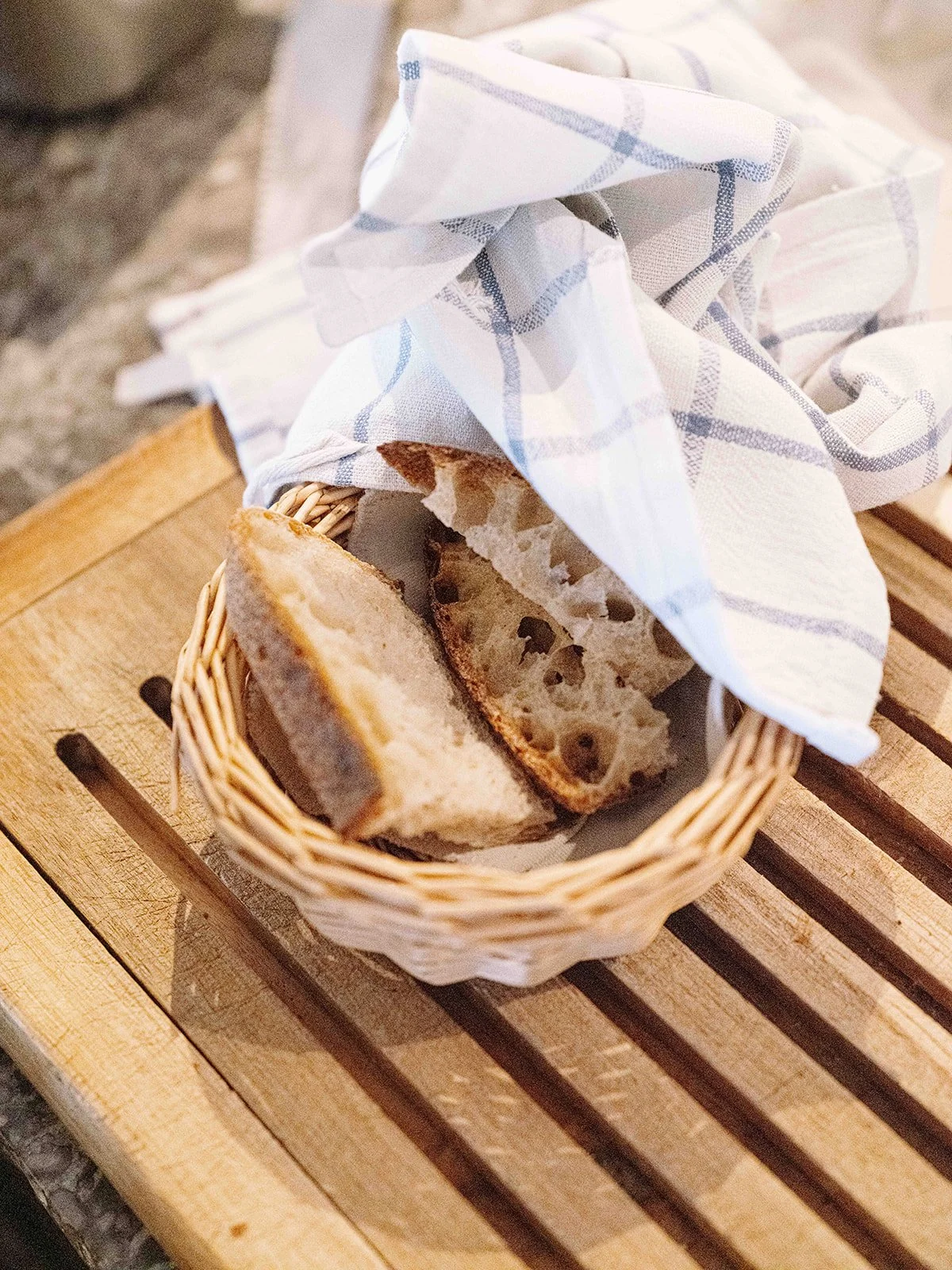 Tranches de pain dans un panier recouvert d'un torchon à carreaux, sur une table en bois.
