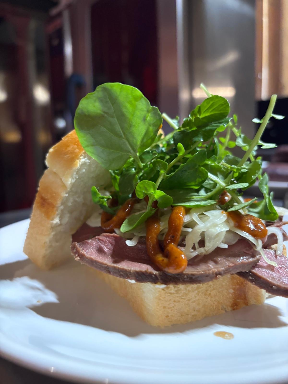 Sandwich avec viande, salade, germes, salade verte et sauce, dans un pain baguette.