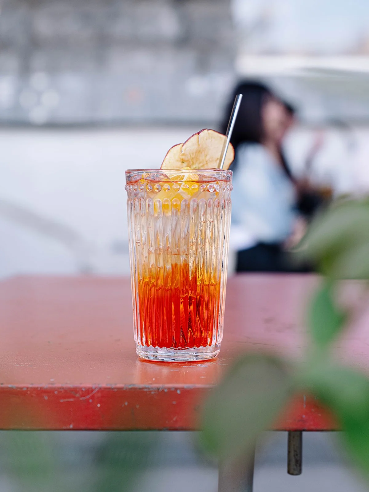 Verre élevé contenant une boisson orangeâtre avec des tranches de pomme et une paille.