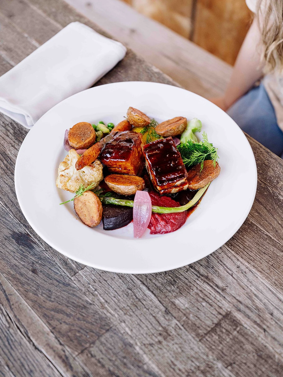 Plat gastronomique avec différents morceaux de viande nappés de sauce, légumes variés, et garnitures colorées, présenté sur une assiette blanche.