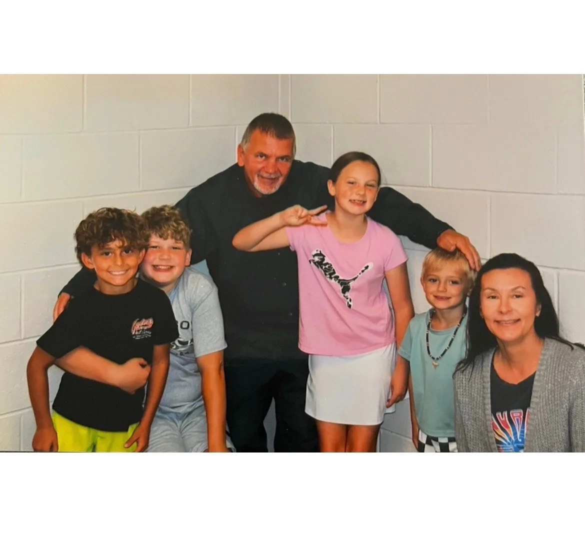 Douglas Vance with four of his grandchildren and his wife Heather, against a painted cinderblock wall