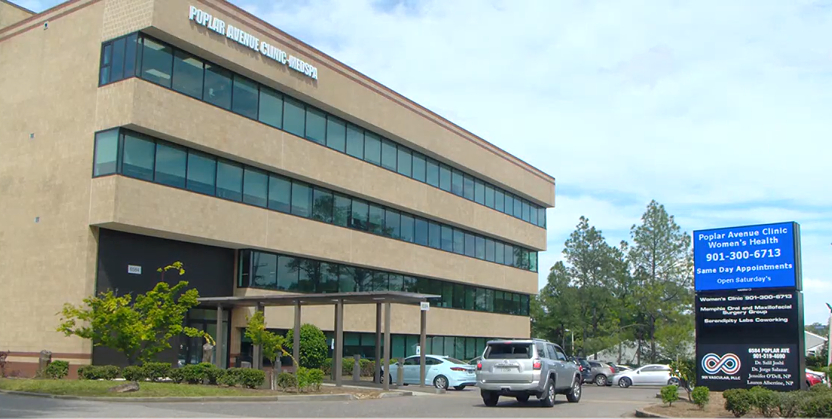 Three-story suburban office building at 6584 Poplar Avenue, Memphis, with a roadside marquee listing the clinic alongside an oral surgery group, a vascular practice and a coworking company