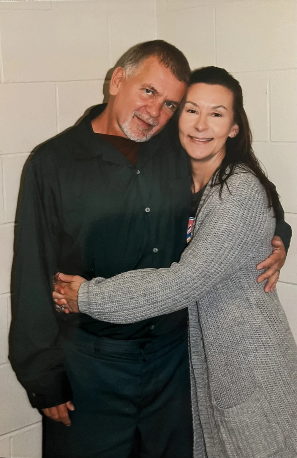 Douglas Vance and Heather, arms around each other, against the same cinderblock wall