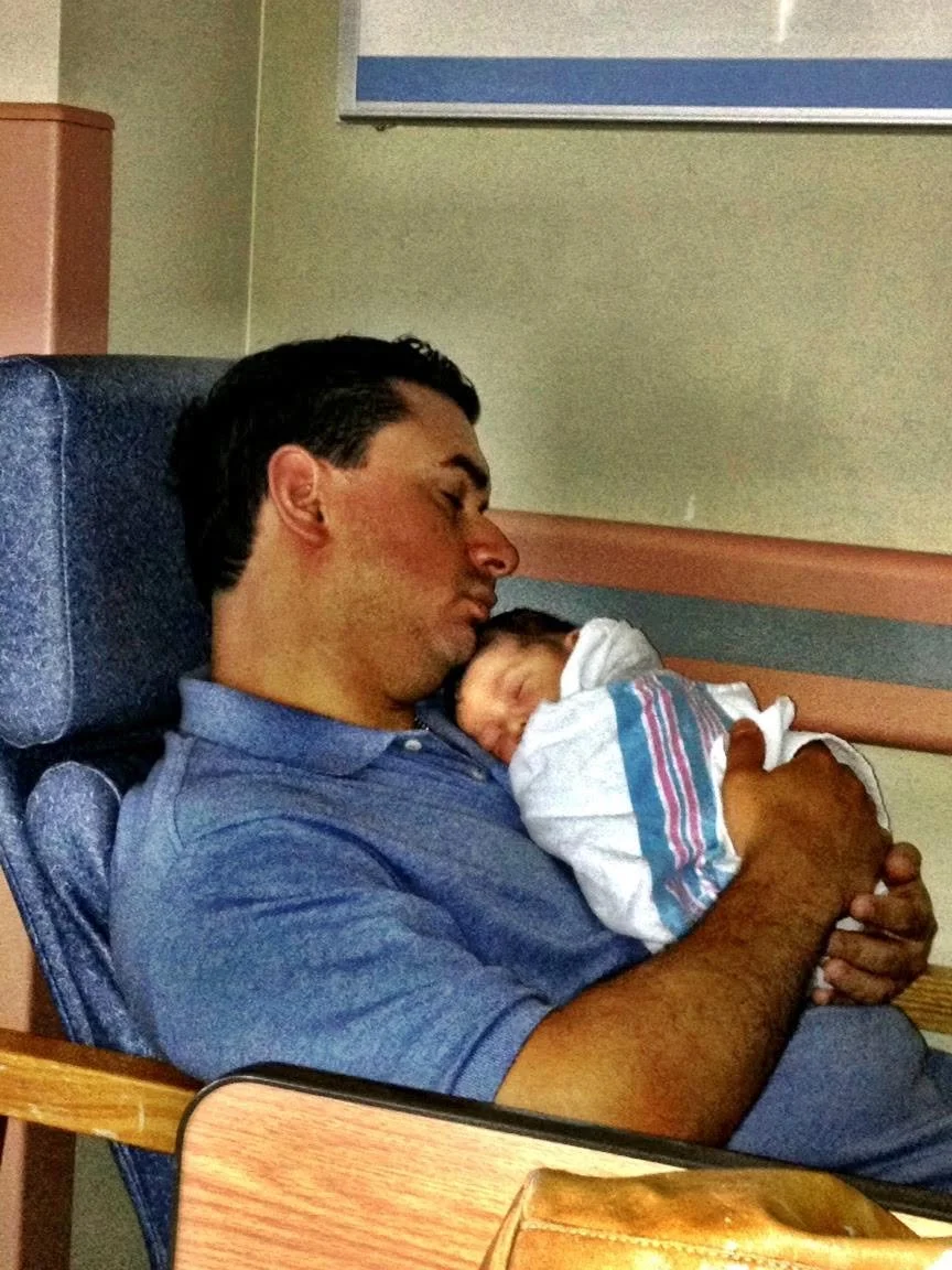 Michael Castillero asleep in a hospital chair with his newborn son on his chest, 2012