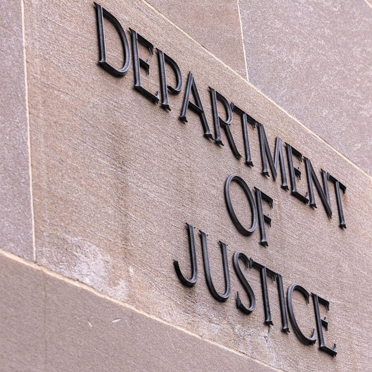 Close-up of a sign on a beige brick wall that reads 'DEPARTMENT OF JUSTICE' in black raised letters.