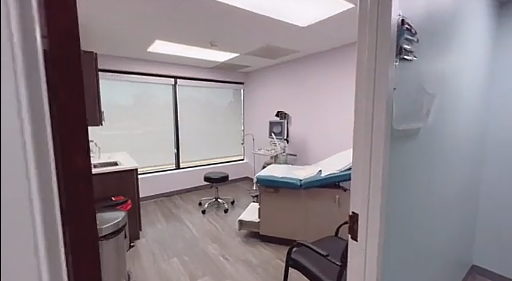 Small clinic exam room with an exam table, a rolling stool, a chair, a sink and a window