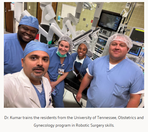 Dr. Kumar in scrubs in an operating room with four University of Tennessee obstetrics and gynecology residents beside a surgical robot.