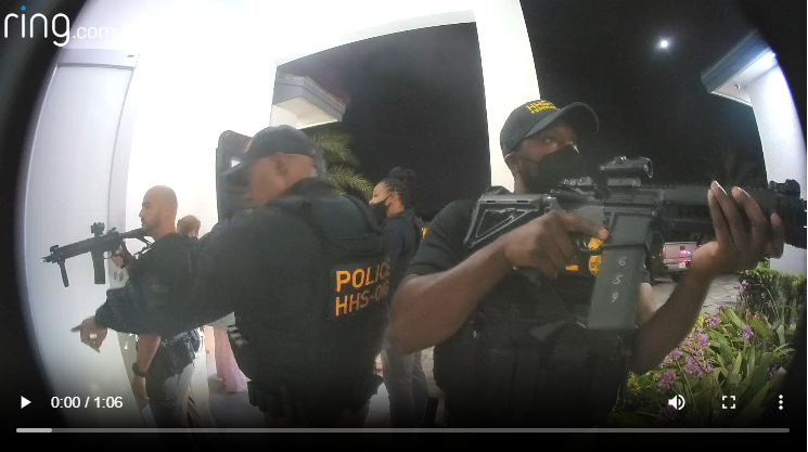 Several police officers in tactical gear, armed with rifles, standing outside a building at night.