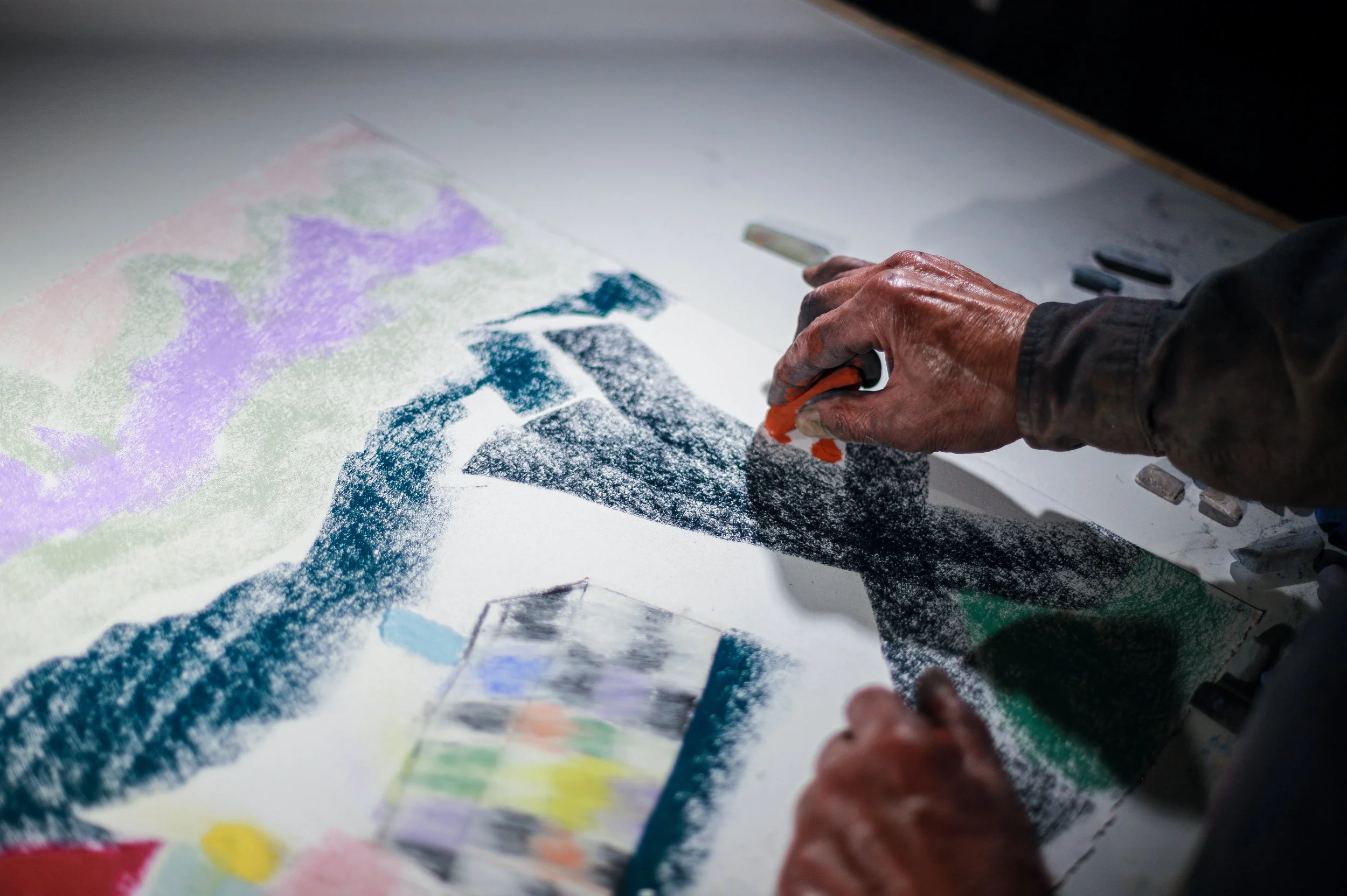 Close-up of a person's hand holding a pencil, working on a colorful abstract art piece on paper, with additional art supplies nearby.