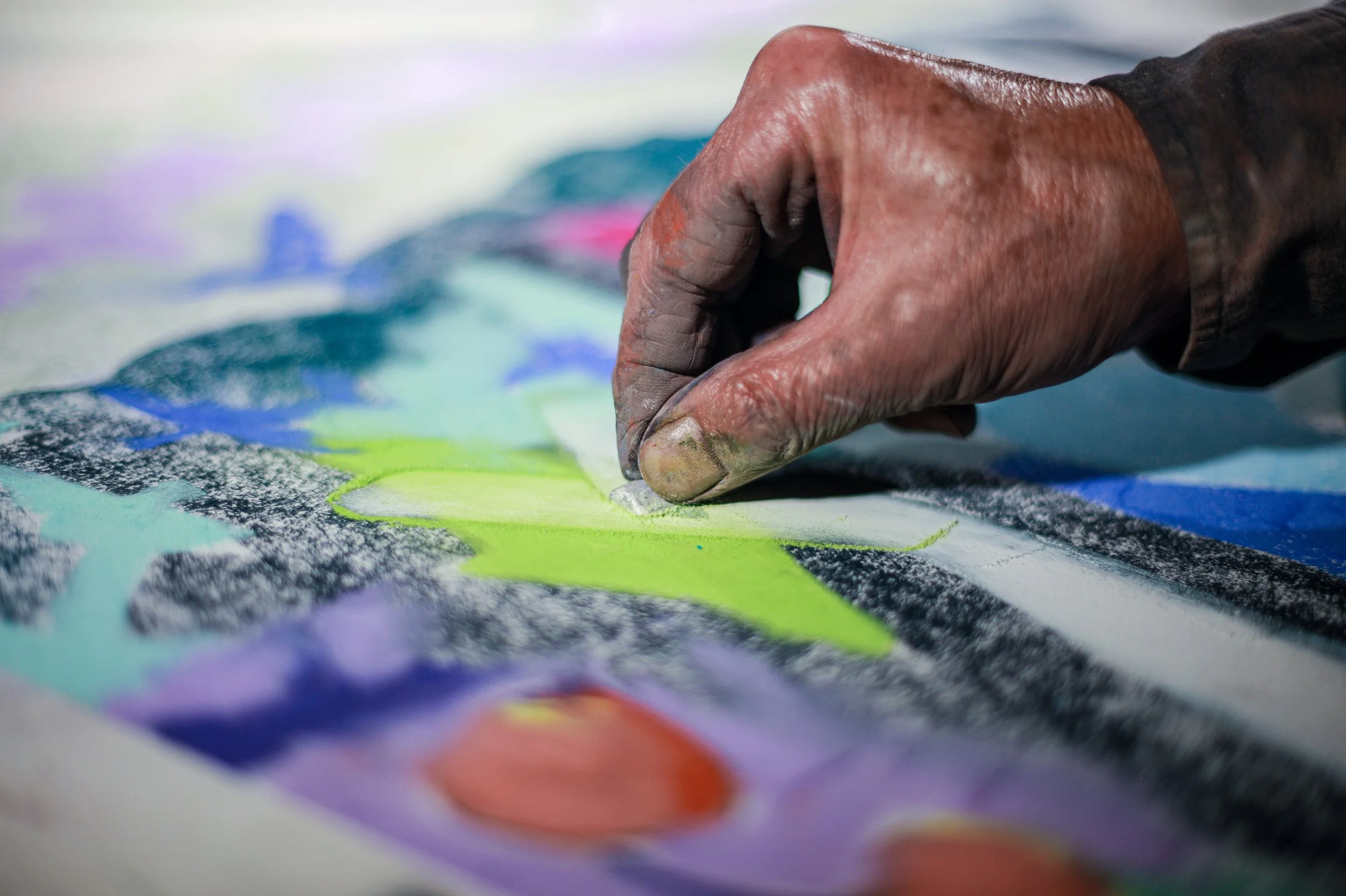 Close-up of a person's hand drawing on a piece of paper with colorful chalks or pastels.