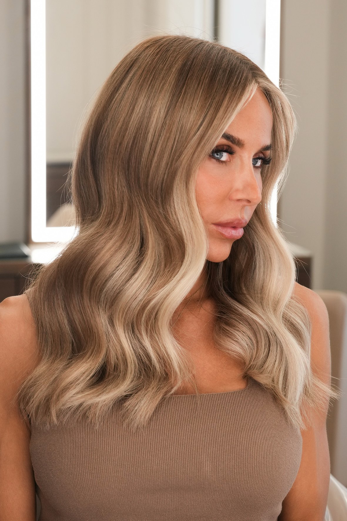 A woman with long, wavy hair, with blonde face framing balayage colour.