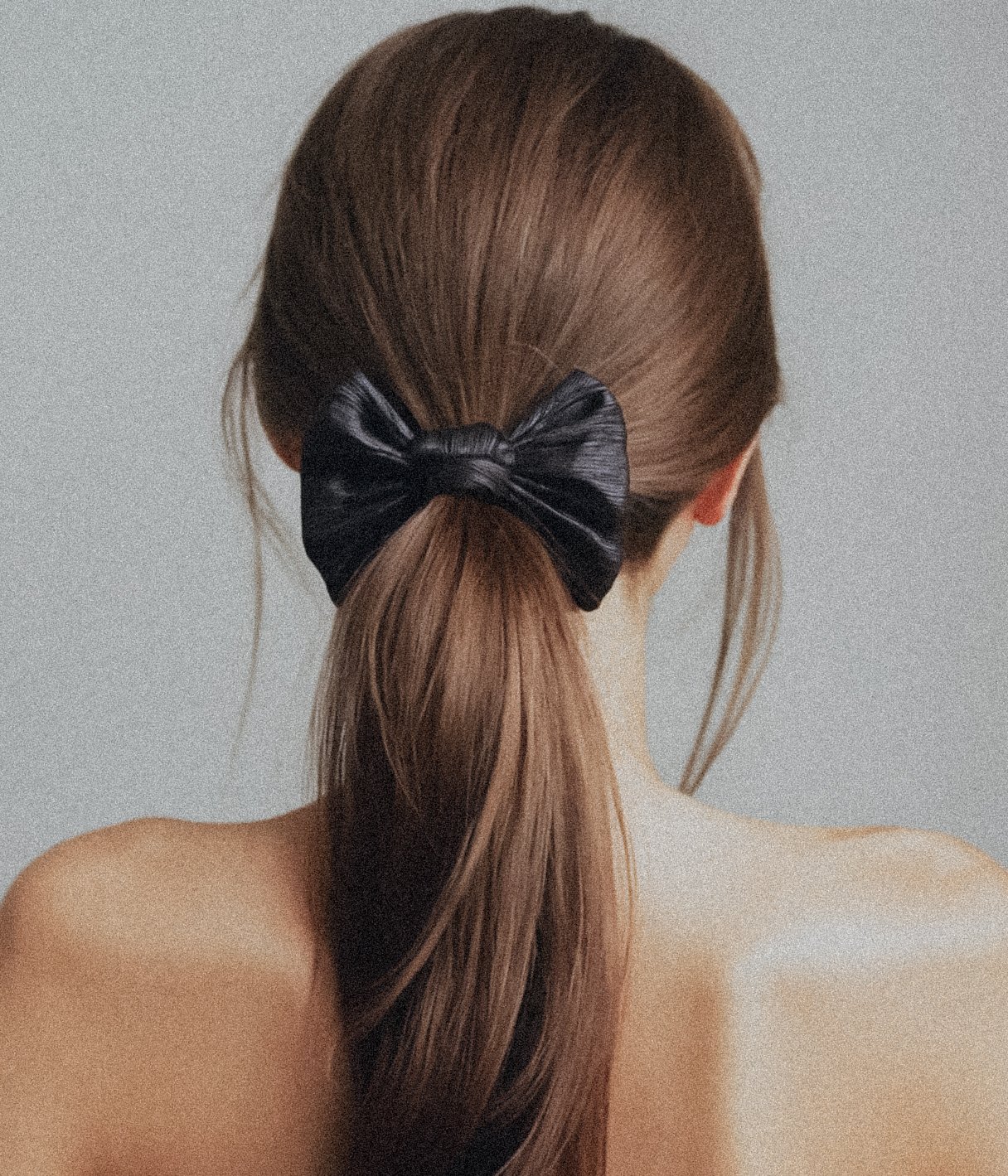 Back of a person's head with long brown hair tied in a ponytail with a black hair bow.