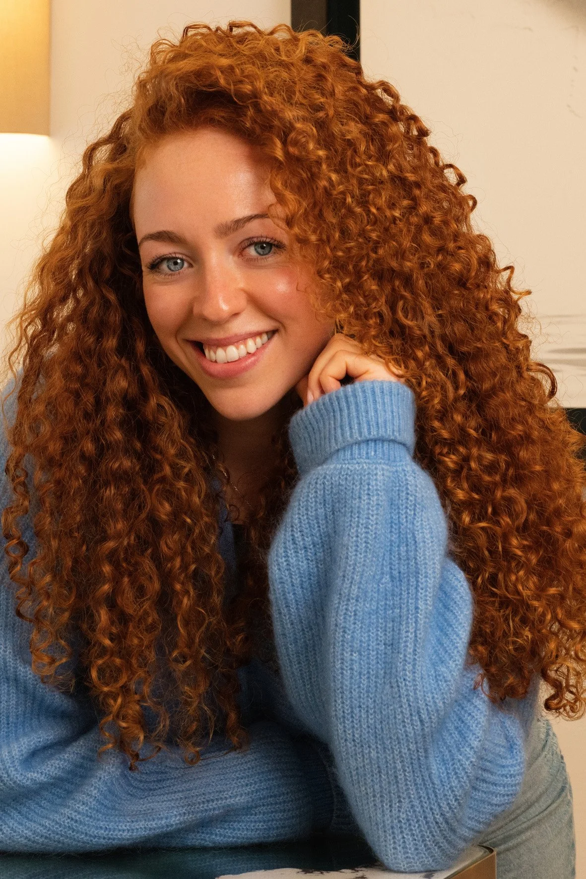 A smiling woman with long, curly red hair styled by the team at The Six, Mayfair.