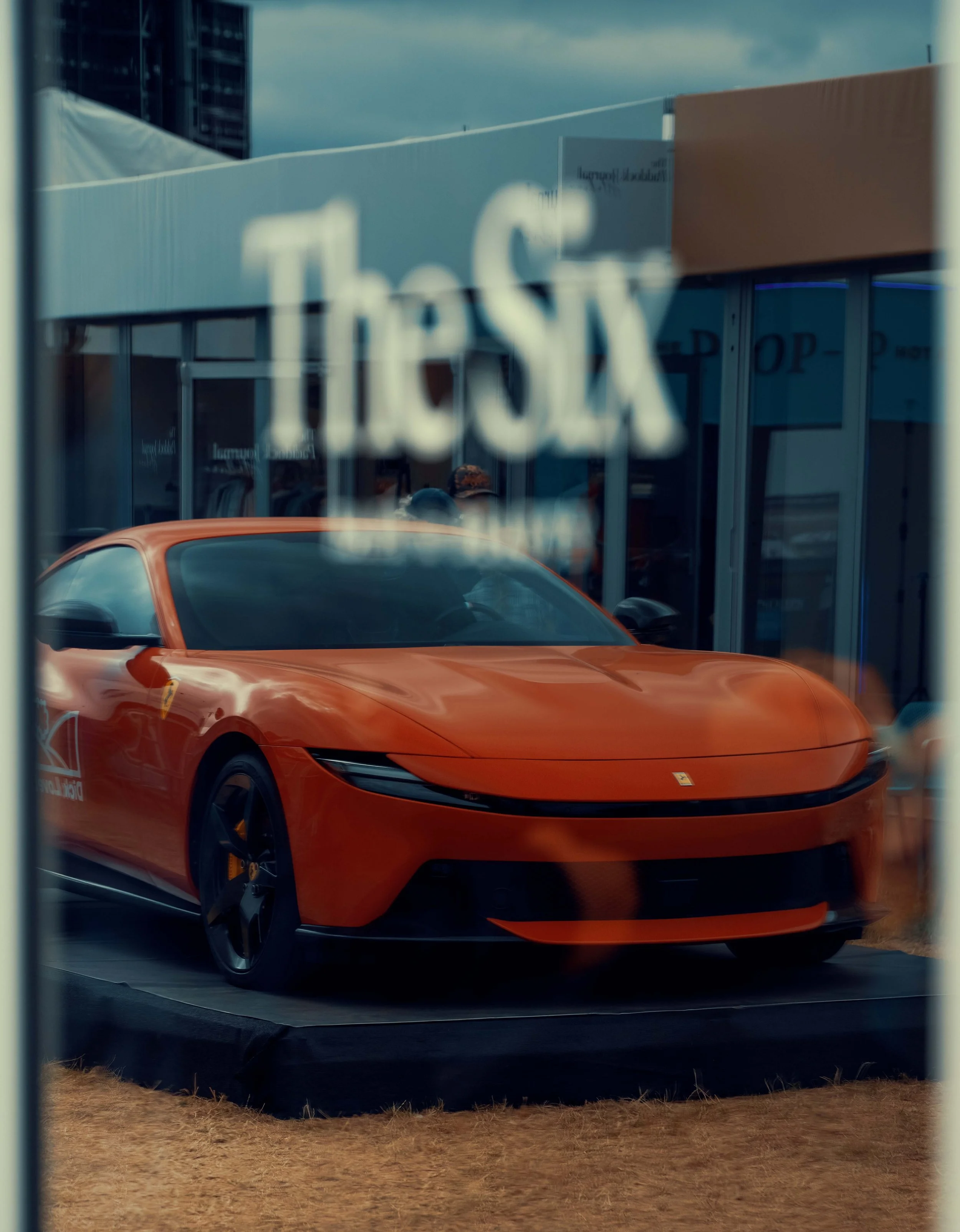 Reflection of a bright orange sports car in a glass window with the word 'Tesla' visible.