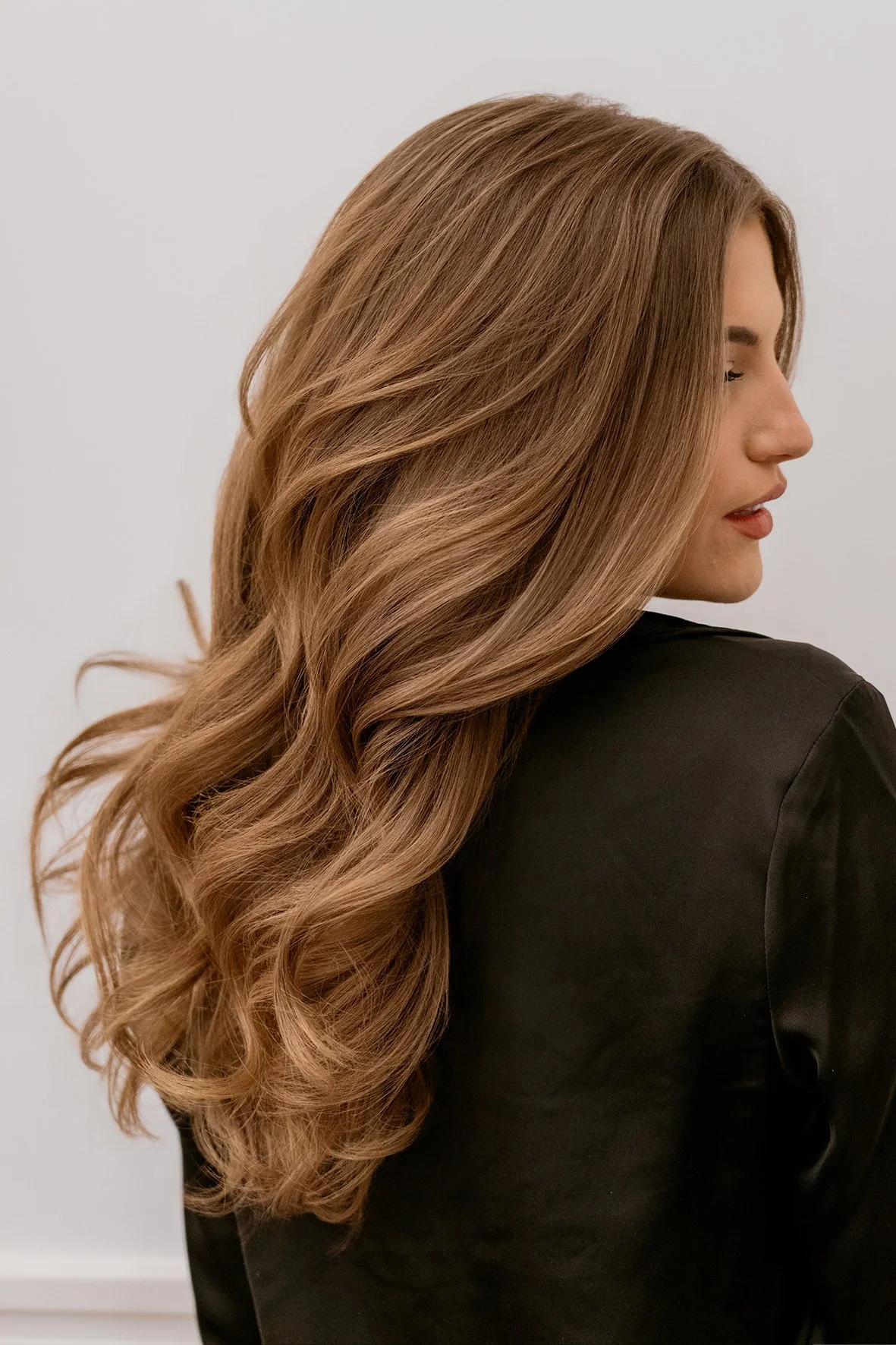 Side view of a woman with long, wavy, warm light brown hair with balayage colour by Milena for extra dimension.
