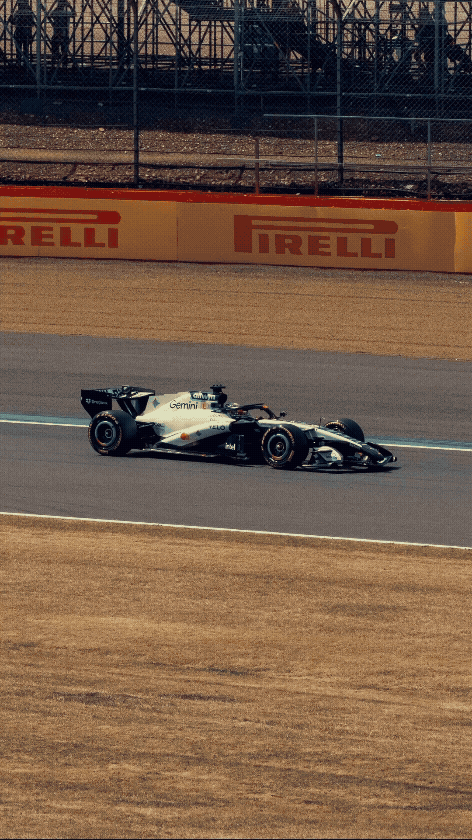 A Formula 1 race car driving on a racetrack with Pirelli advertising banners and fencing in the background.