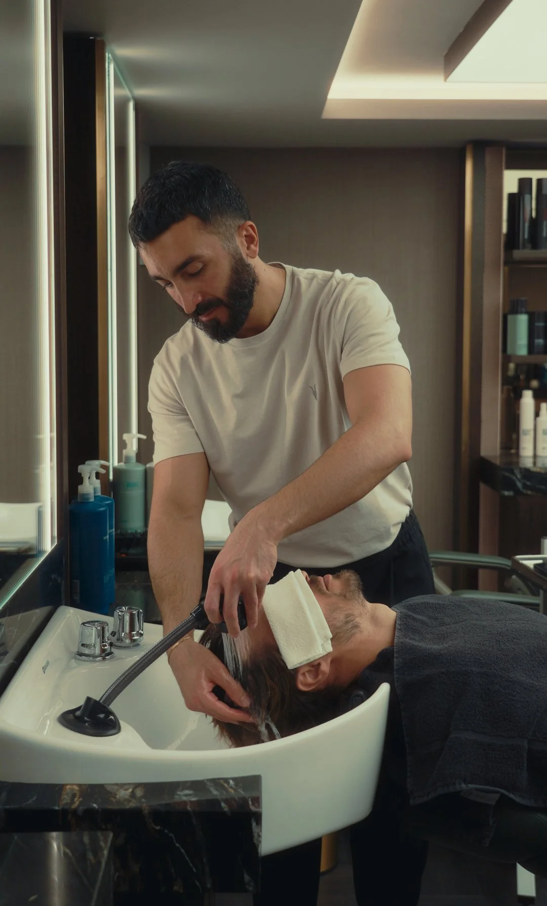 Barber washing a male client's hair in a salon sink.