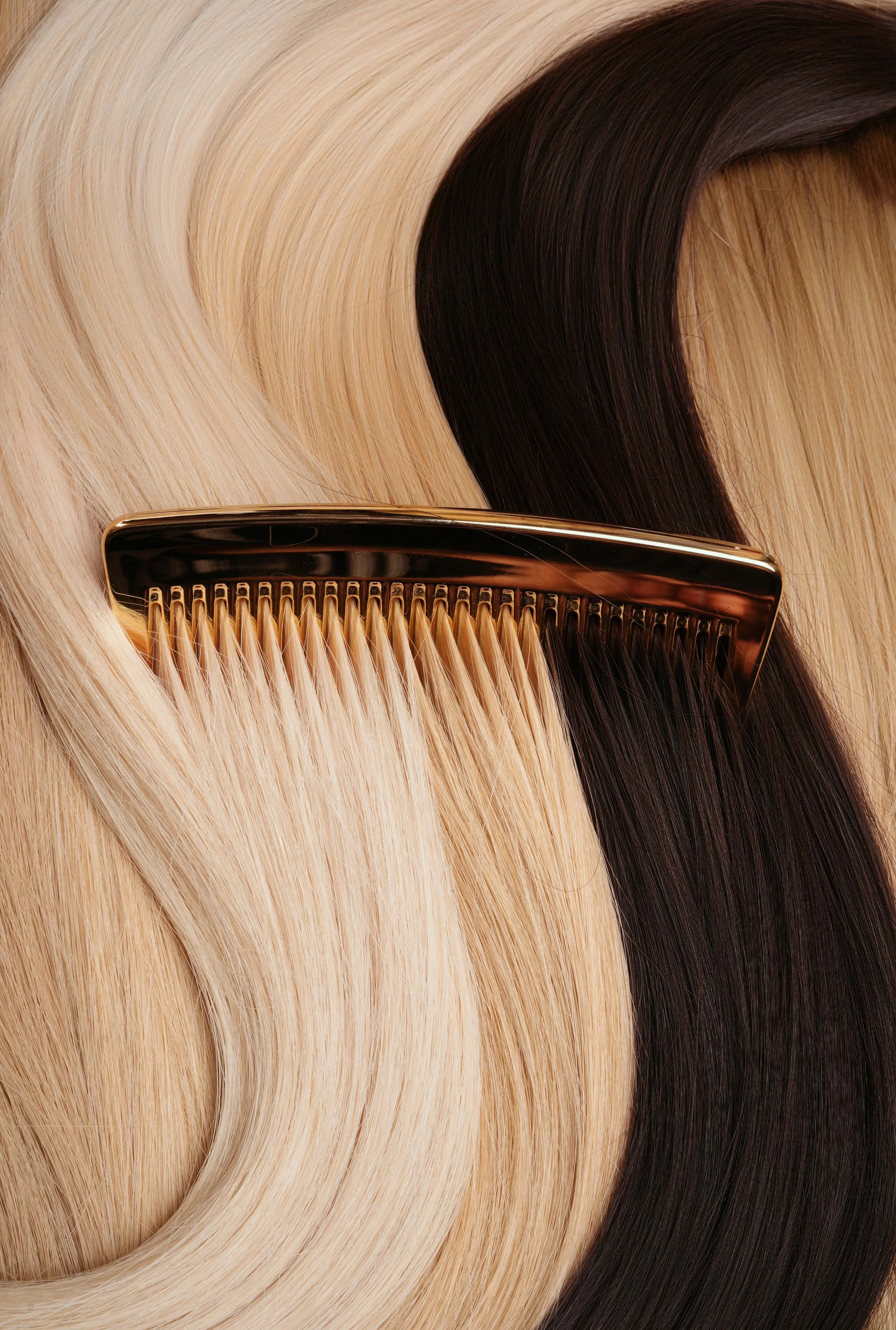 Close-up of a hair comb on strands of blonde and brunette hair extensions.