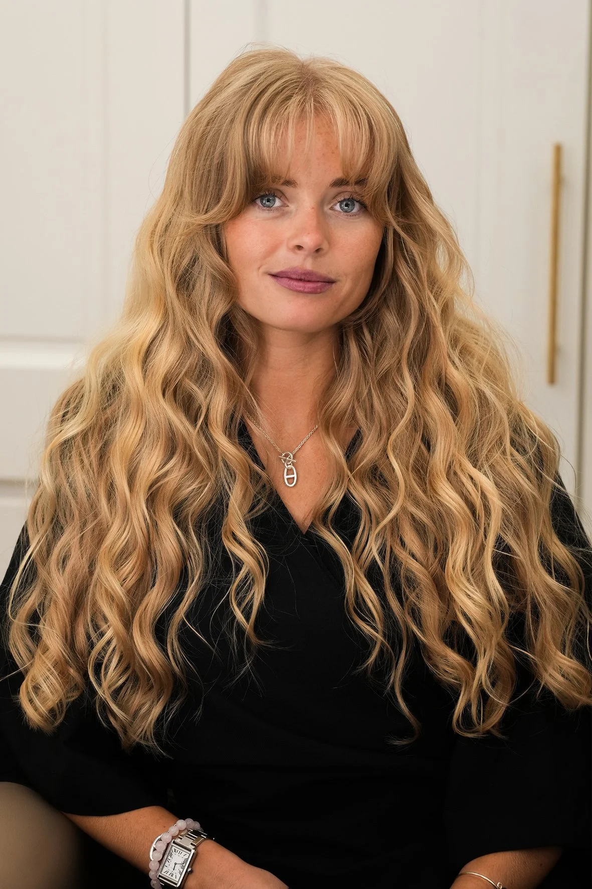 A woman with long, wavy blonde coloured  hair, and a soft fringe.