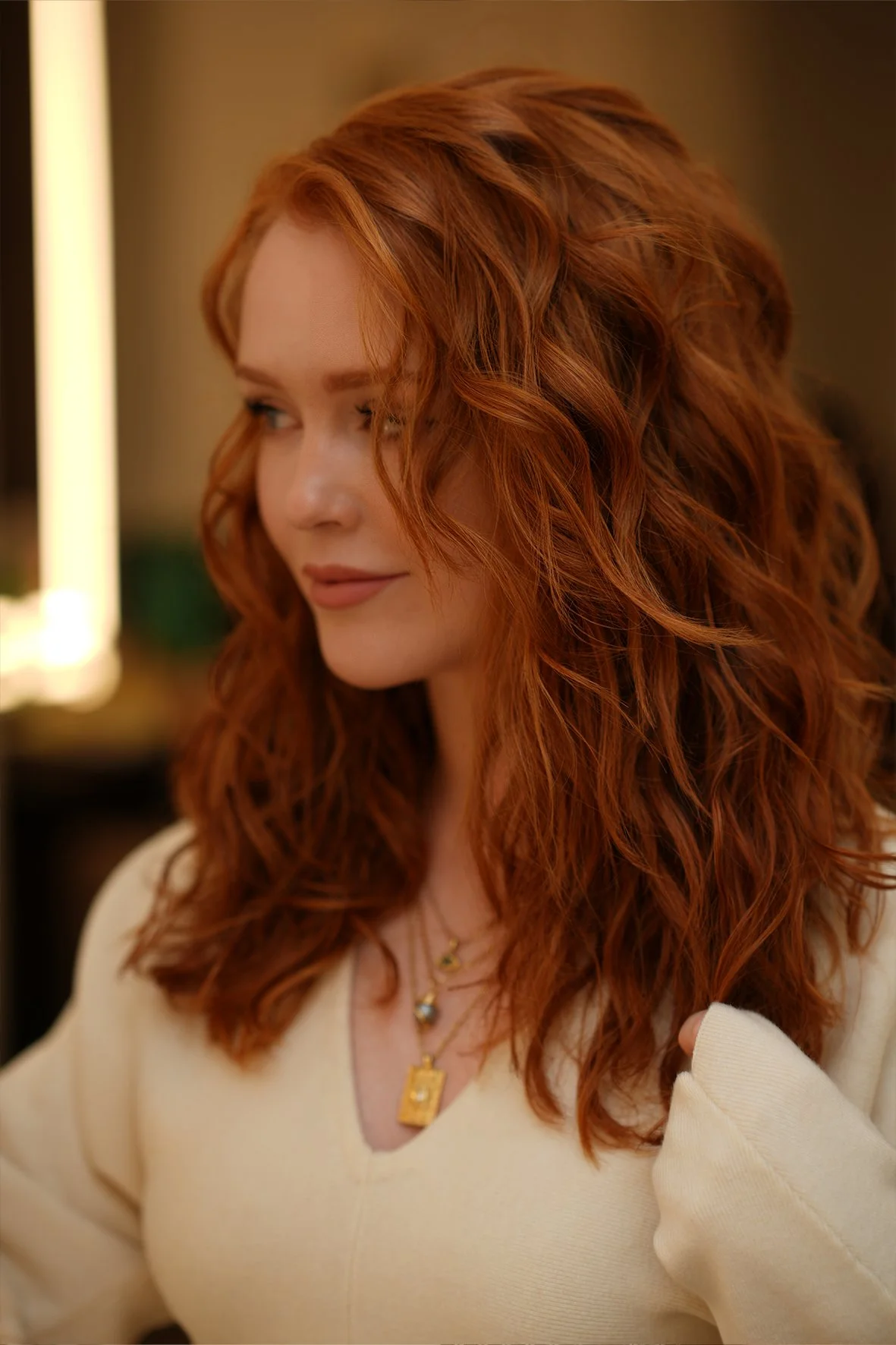 A woman with long, curly red copper coloured hair looking to the side.