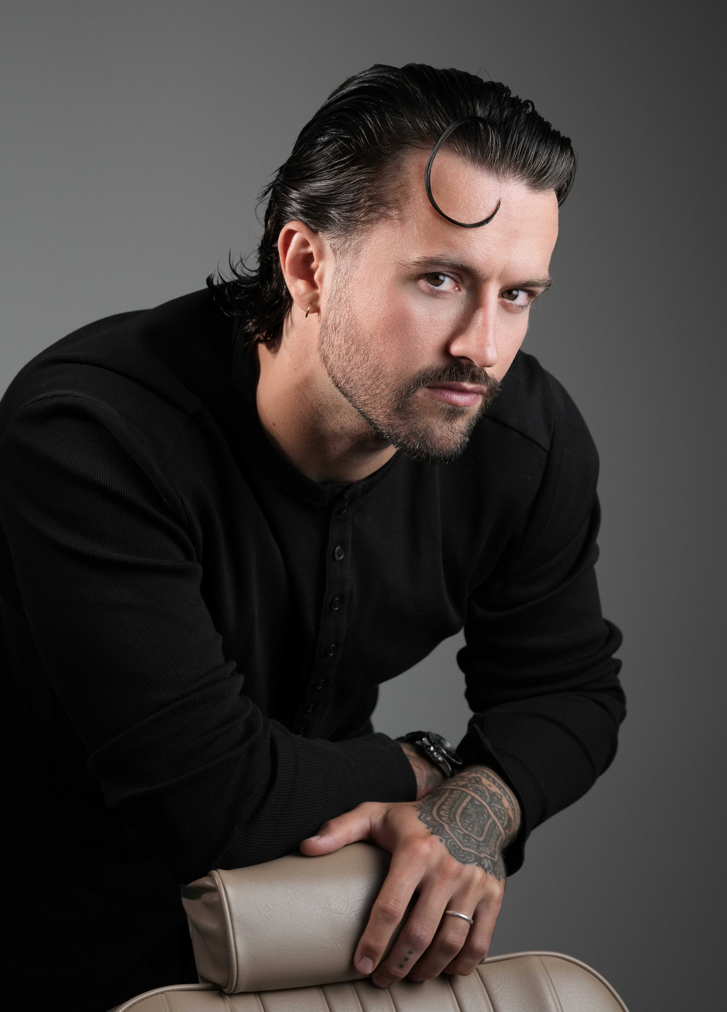 A young man with dark, slicked-back hair and beard groomed.