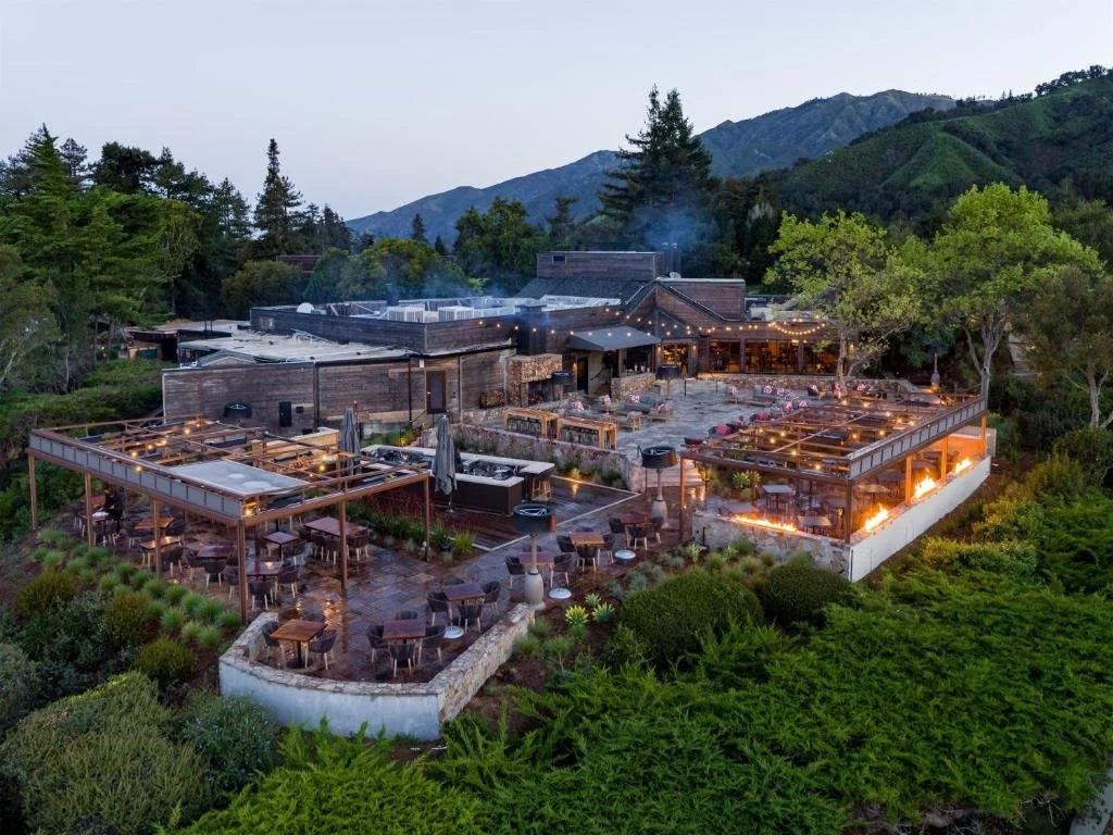 Ventana, Big Sur. A large outdoor restaurant and bar designed by Kipp Stewart. With string lights, surrounded by lush trees and mountains in the background, taken during dusk.