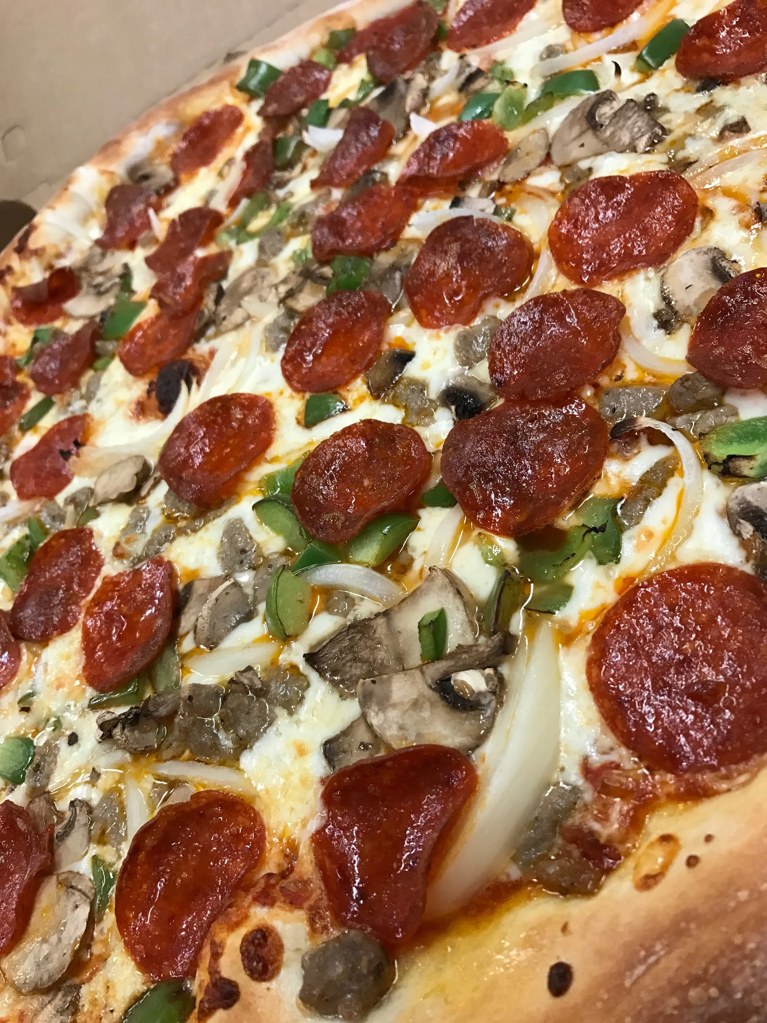 Close-up view of a pepperoni pizza with green peppers, mushrooms, and sausage slices.