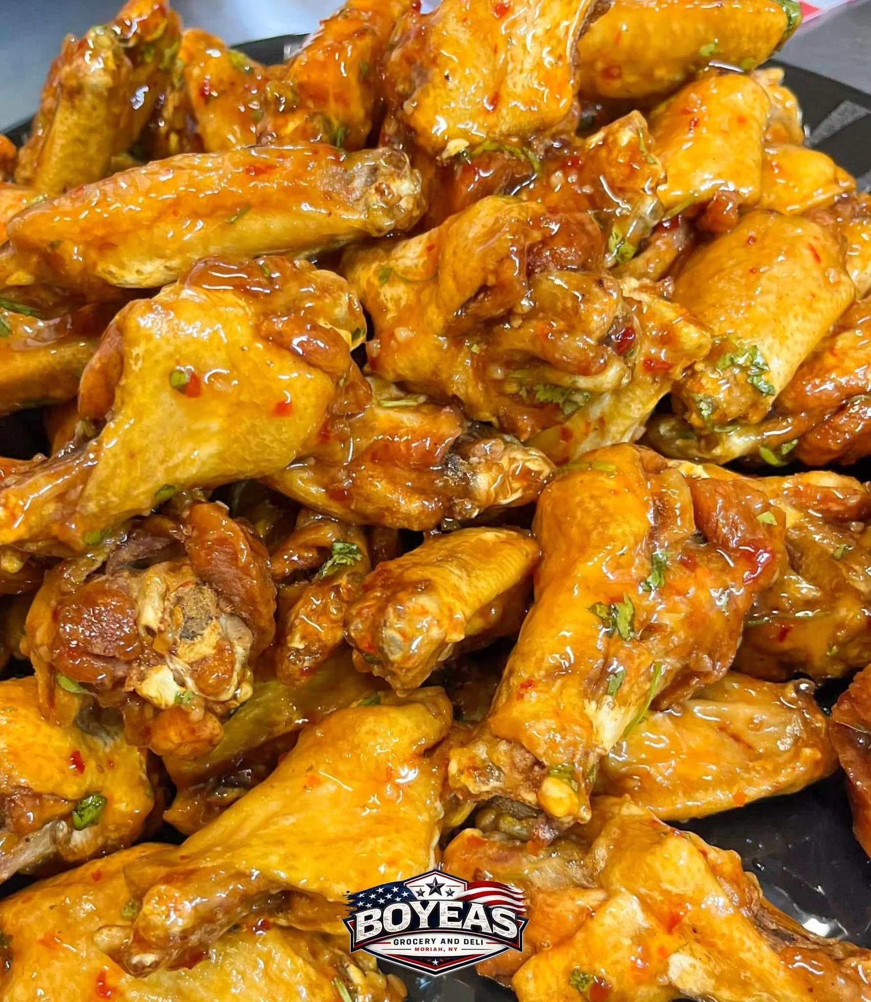 Close-up of glazed fried chicken wings with sauce and herbs on a black platter, with a Boyeas Grocery and Deli logo at the bottom.