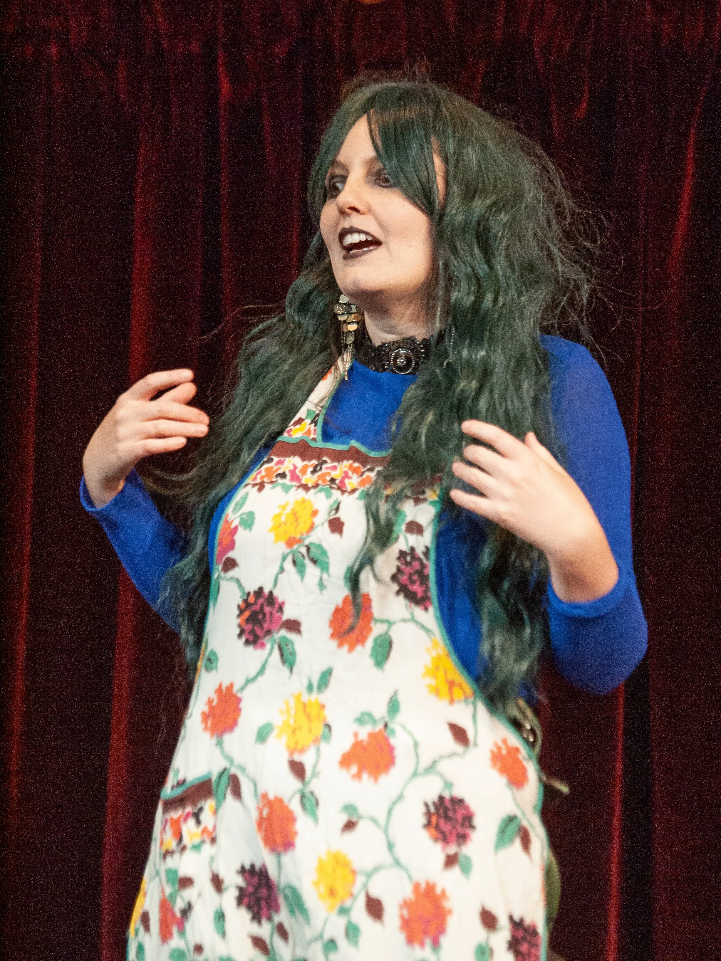 Christina has black lips a green wavy long wig and an apron. She looks a bit spaced out.
