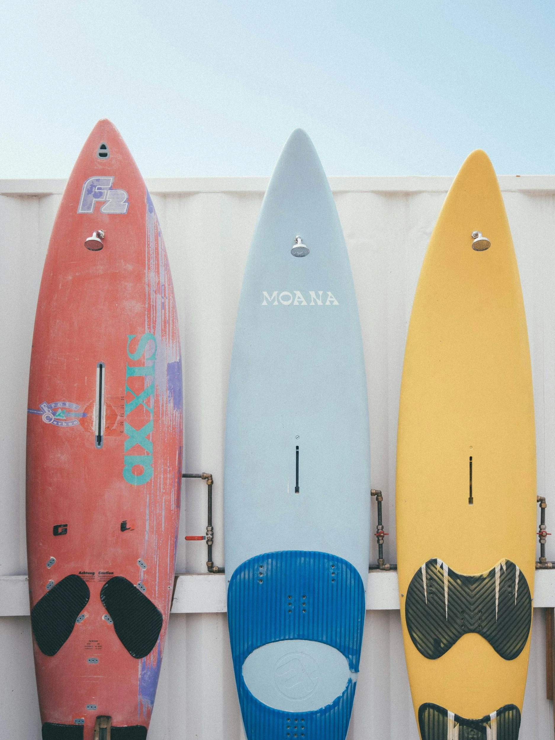 Three surfboards leaning against a white wall, each with a foot paw print traction pad at the bottom.