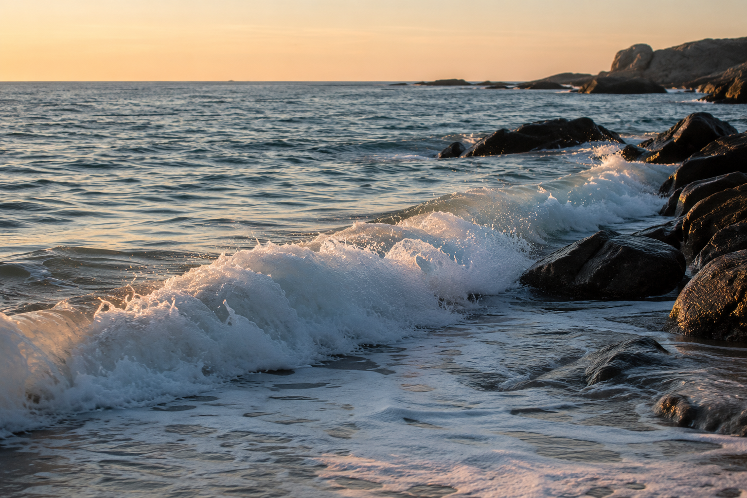 Waves crashing onto a rocky shoreline during sunset at the beach.
