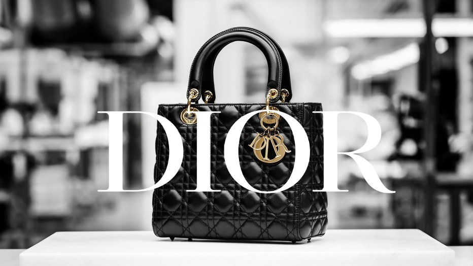 Black quilted Dior handbag with gold hardware and logo, displayed on a white surface in a retail store, with a blurred background.