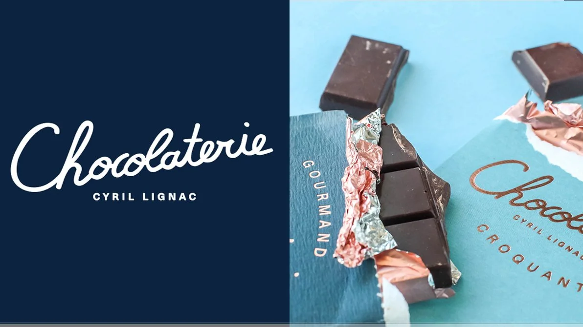 A side-by-side image of a dark blue box with white cursive text reading 'Chocolaterie' and a partially unwrapped chocolate bar on a blue background with similar branding.
