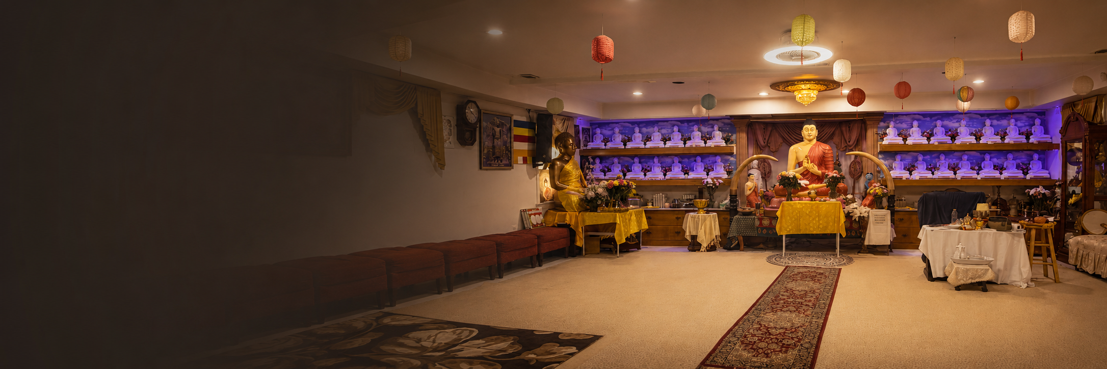 A Buddhist altar room with statues, flowers, and offerings, decorated with colorful paper lanterns hanging from the ceiling.