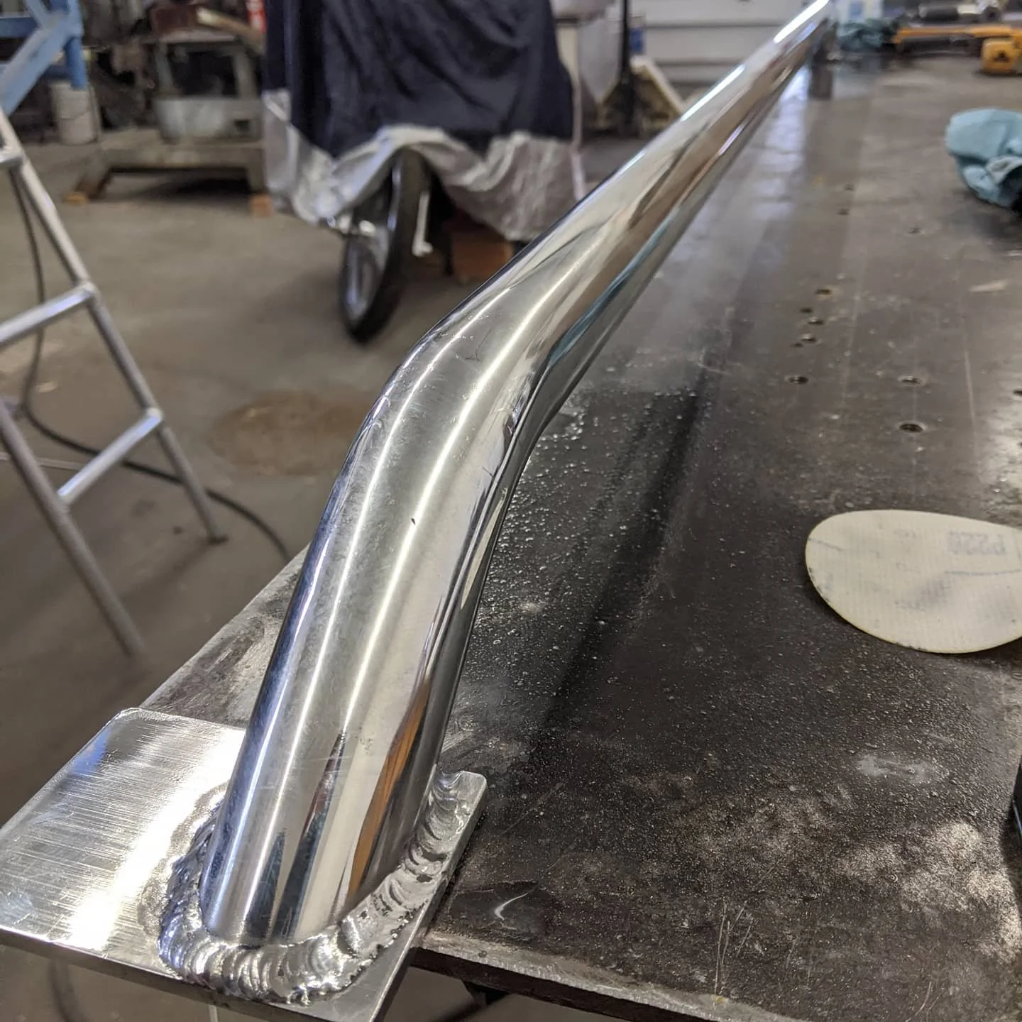 Close-up of a shiny, welded metal tube on a workbench in a workshop.