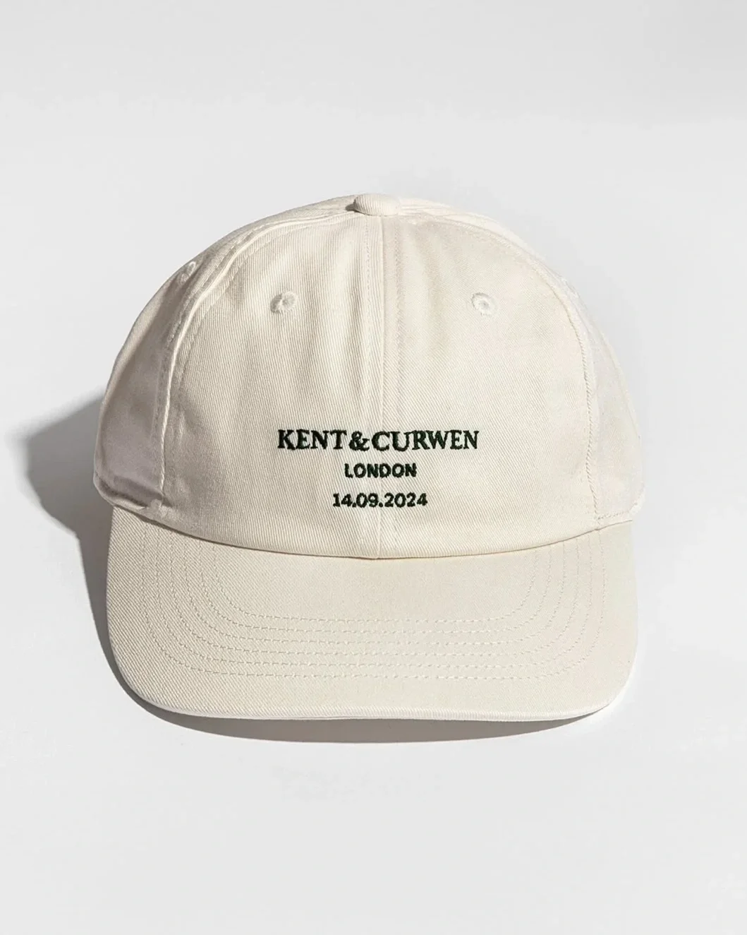 A white baseball cap with black embroidered text that reads 'KENT & CURWEN LONDON 14.09.2024'.