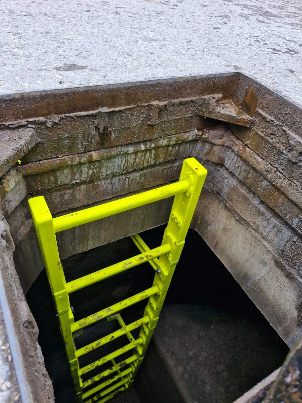 A bright yellow ladder leading into a large underground hole with brick and concrete walls.