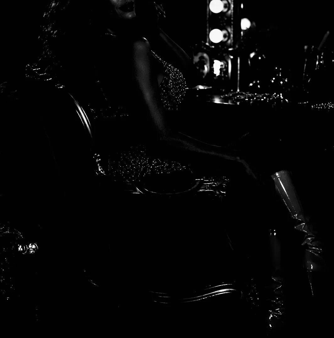 Silhouette of a woman sitting on a chair in a dressing room with illuminated vanity lights in the background.