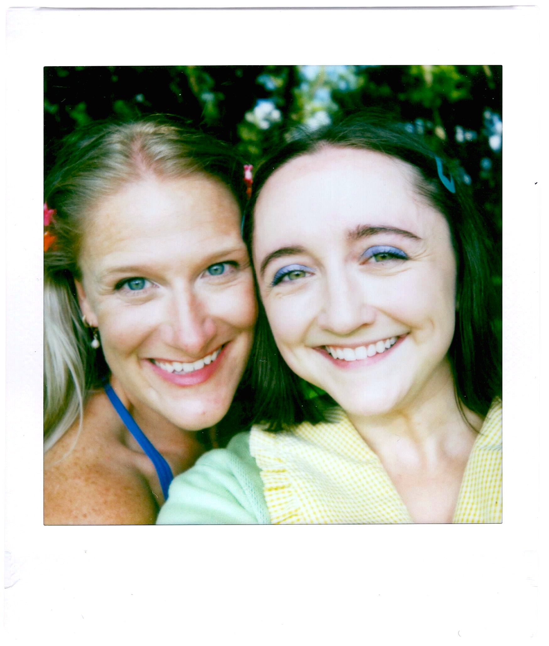 Close-up of two women smiling outdoors, with trees in the background.